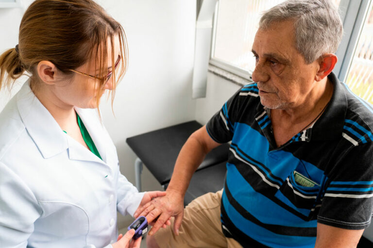 Uma médica mede os batimentos cardíacos de um senhor idoso. Observatório da APS - DCNTs